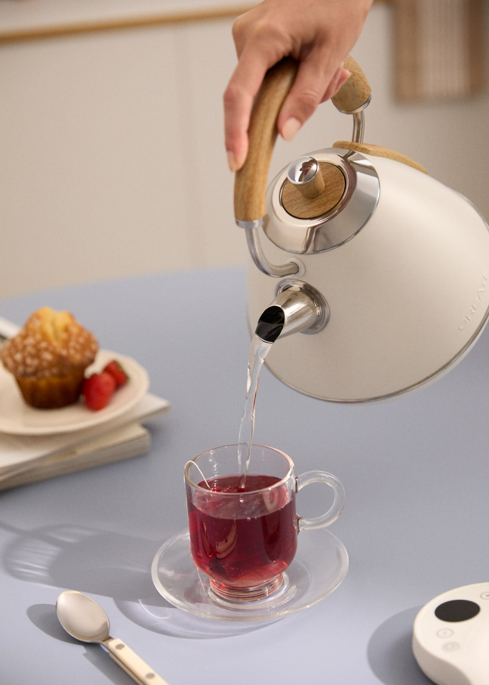 Una mano vierte agua de una tetera blanca con mango de madera en una taza de té.