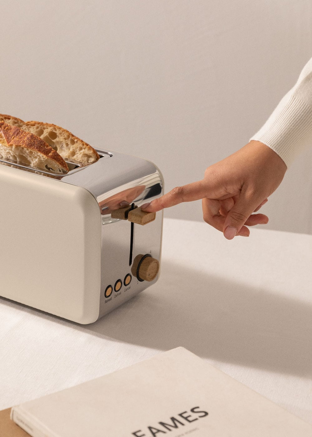 Una mano presiona una palanca en una tostadora crema y cromo con pan dentro.