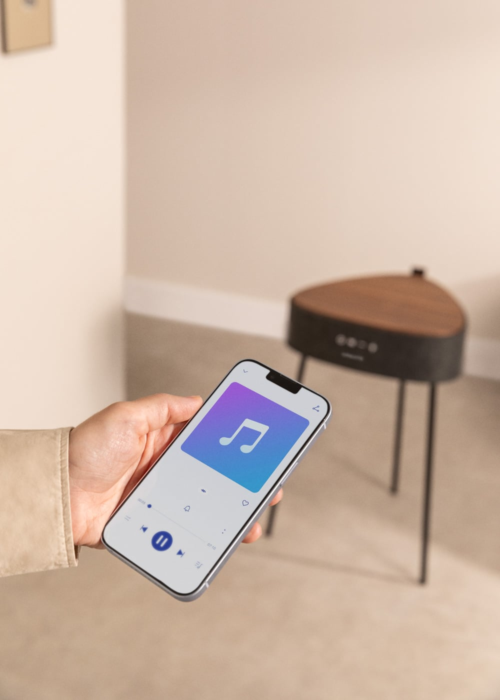 Una mano sostiene un smartphone con app de música. Un altavoz está de fondo.