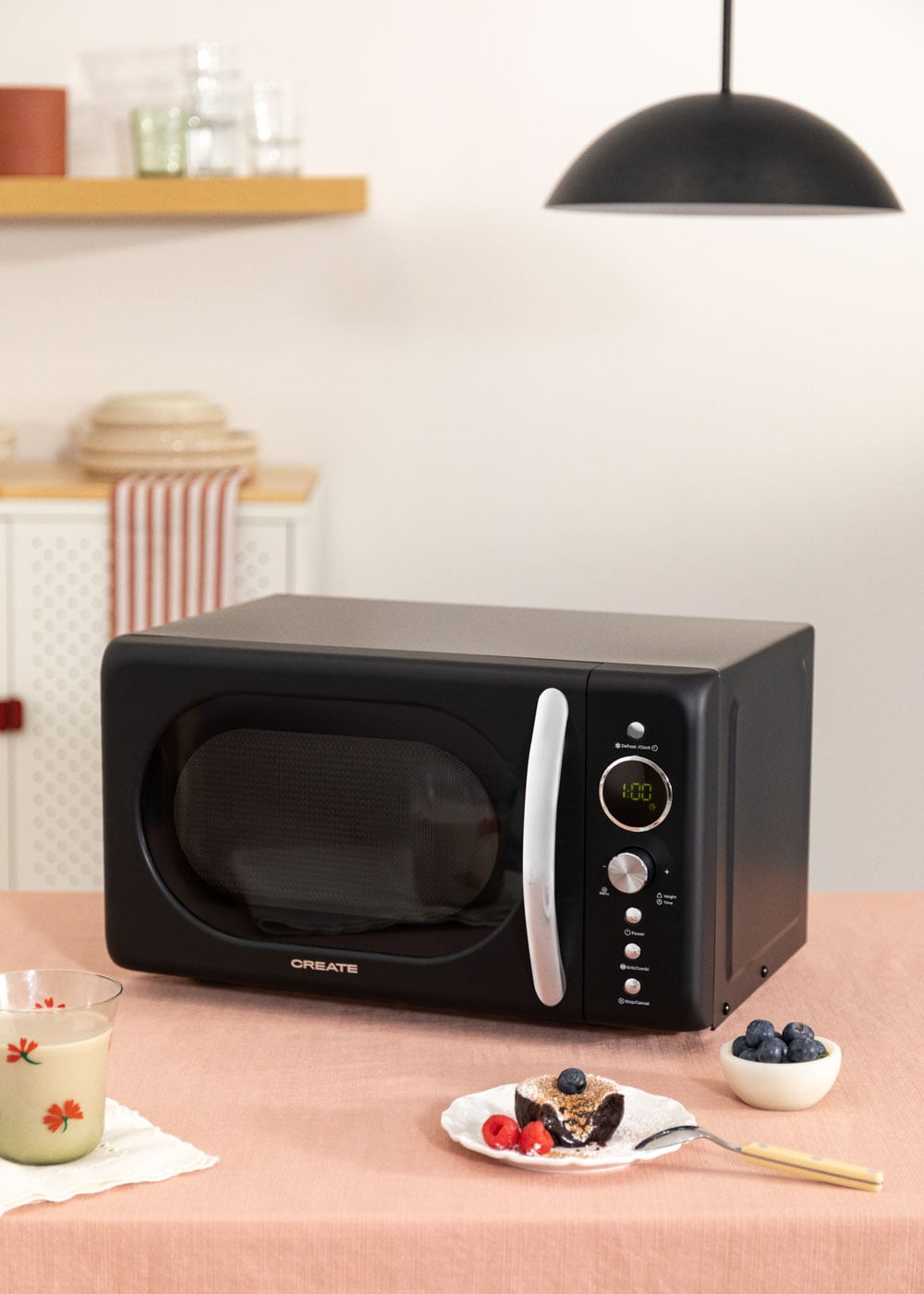 Un micro-ondes noir sur une nappe rose avec gâteau, baies et boisson.