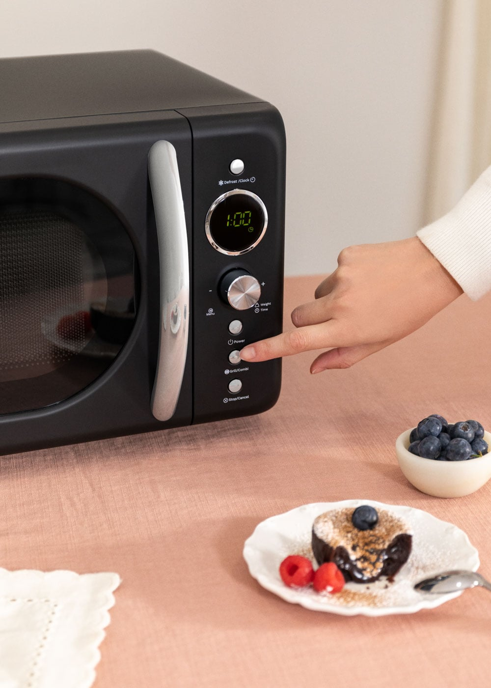 Micro-ondes noir avec écran numérique, à côté un dessert aux baies.