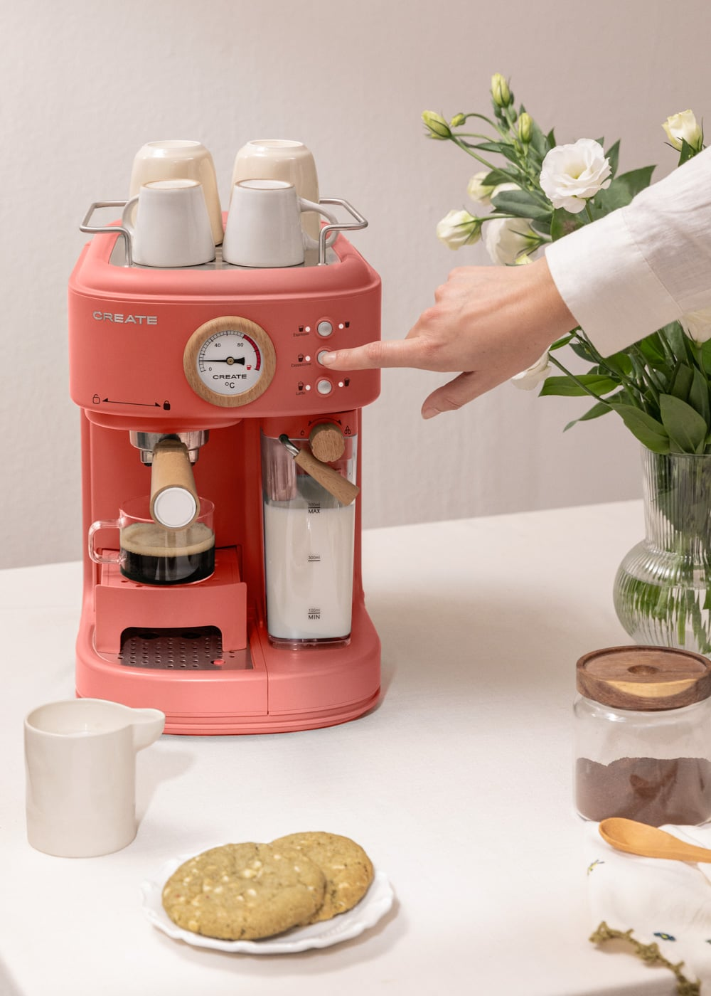 Una persona presiona un botón en una cafetera roja con leche espumosa y espresso.