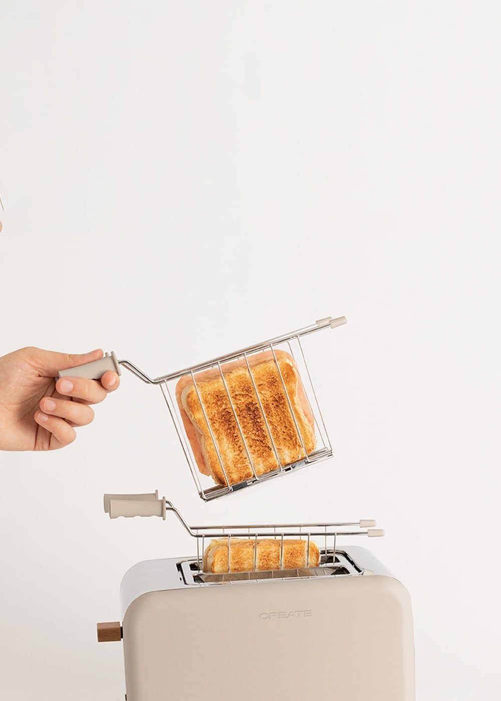 Una mano sostiene una cesta de tostadora con pan tostado sobre una tostadora.