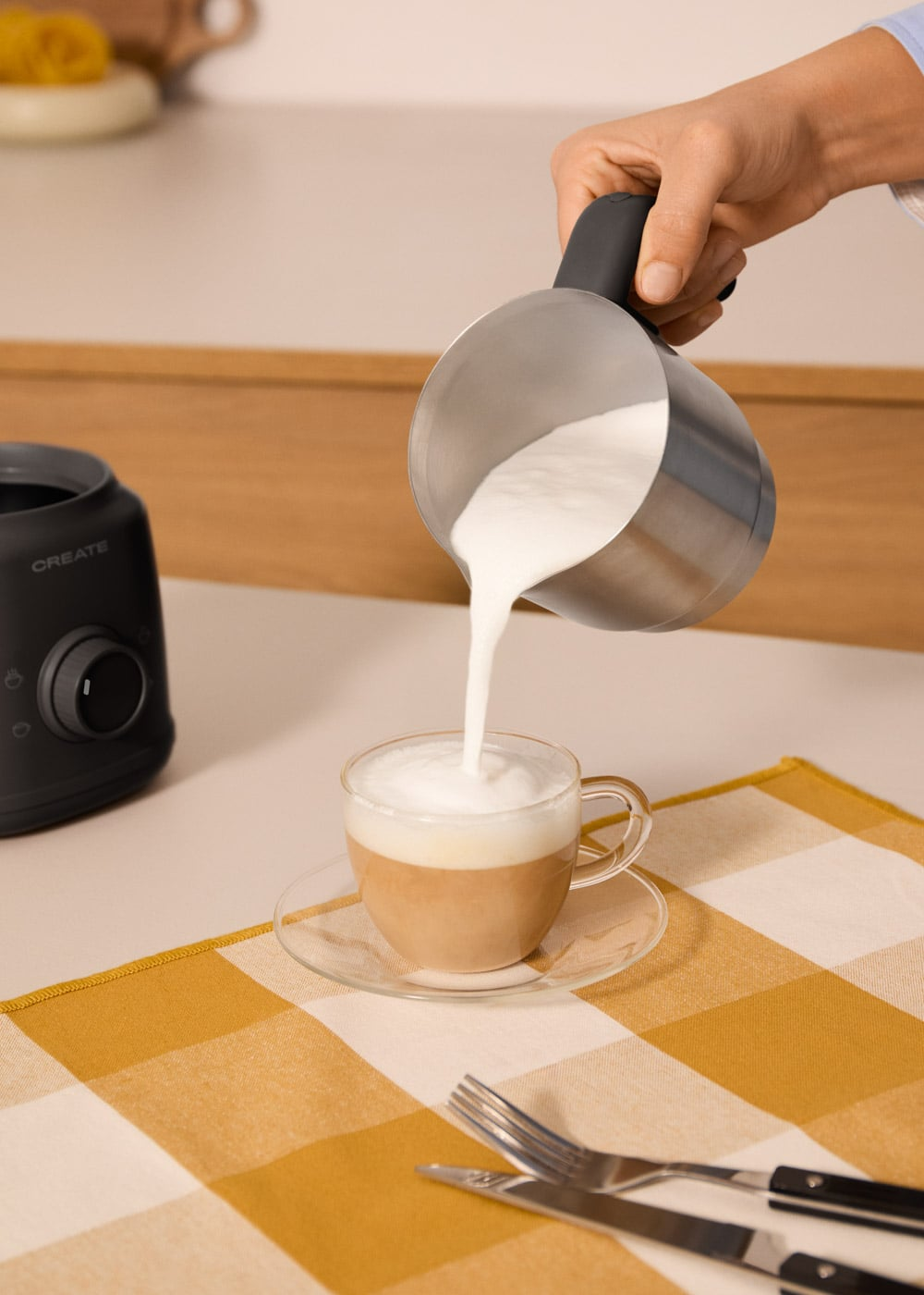 Se vierte leche de una jarra metálica en una taza de café de cristal.