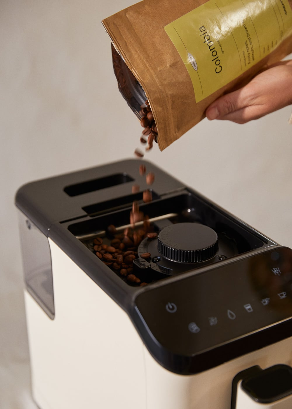 Una mano vierte granos de café de una bolsa marrón en un molinillo de café.