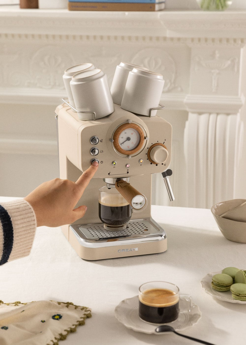 Una mano presiona un botón en una cafetera espresso color crema que prepara café.