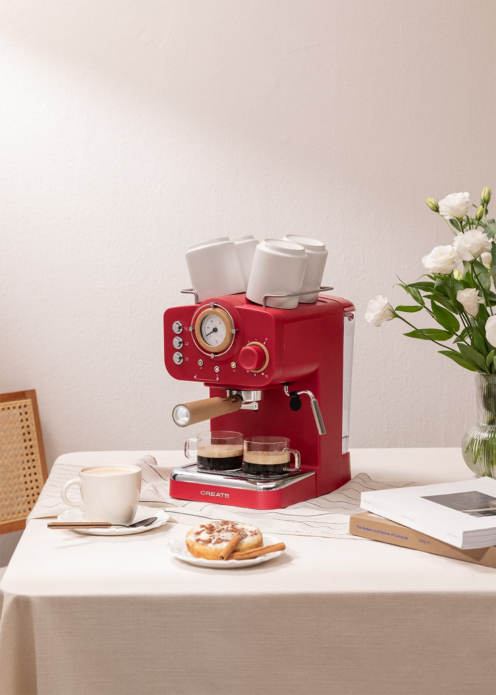 Máquina de espresso roja con dos vasos de espresso, una taza de café, pasteles y flores.