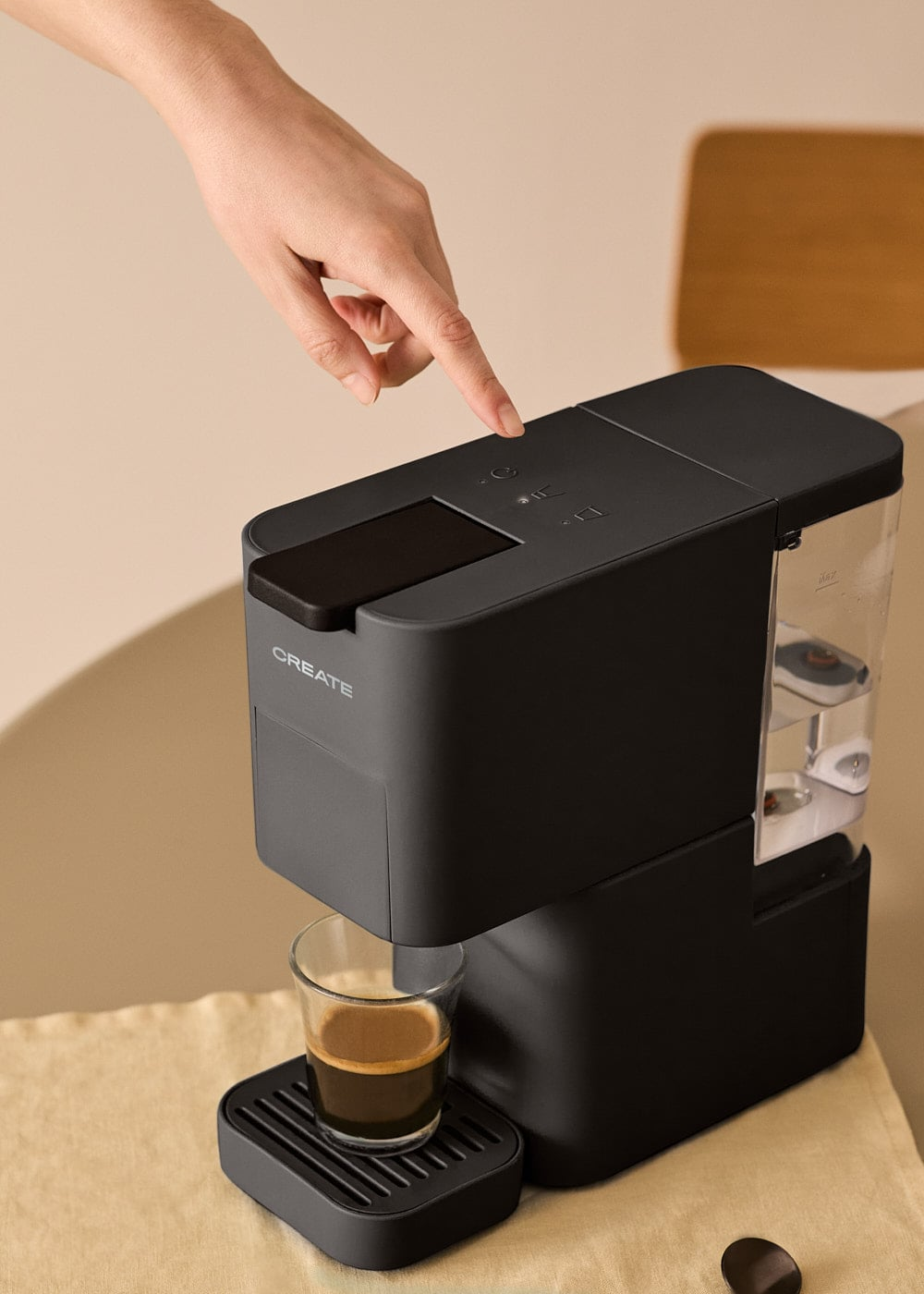 Una mano presiona el botón de una cafetera negra, con un espresso en un vaso.