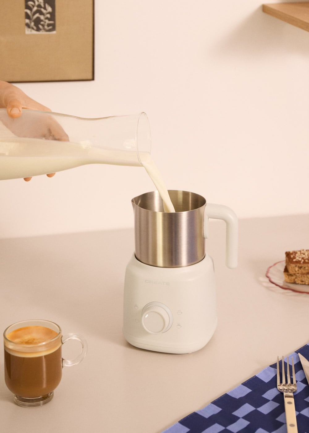 La leche se vierte de una jarra de vidrio a un espumador de leche blanco.