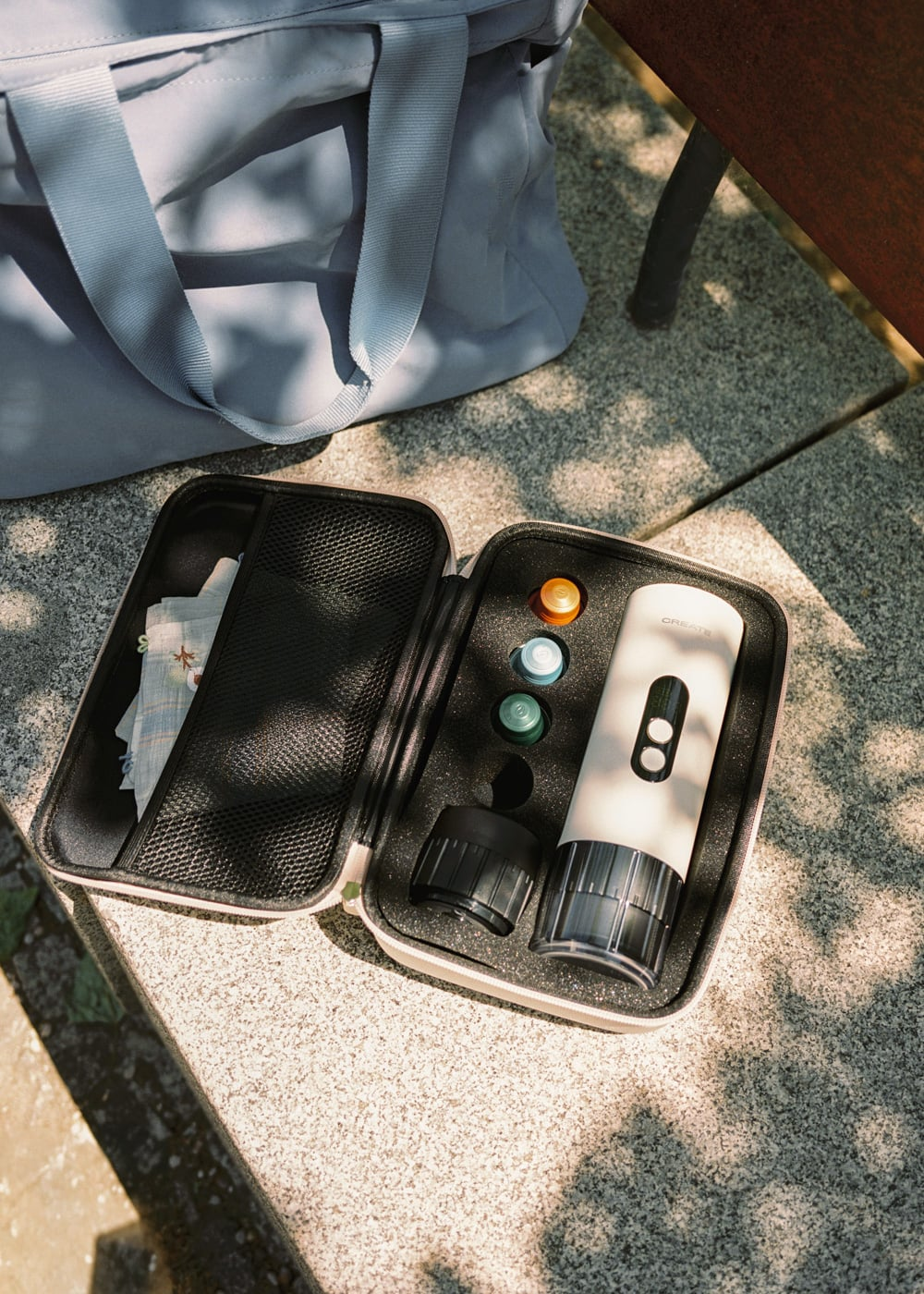 Un estuche beige claro con cafetera, cápsulas y paño.
