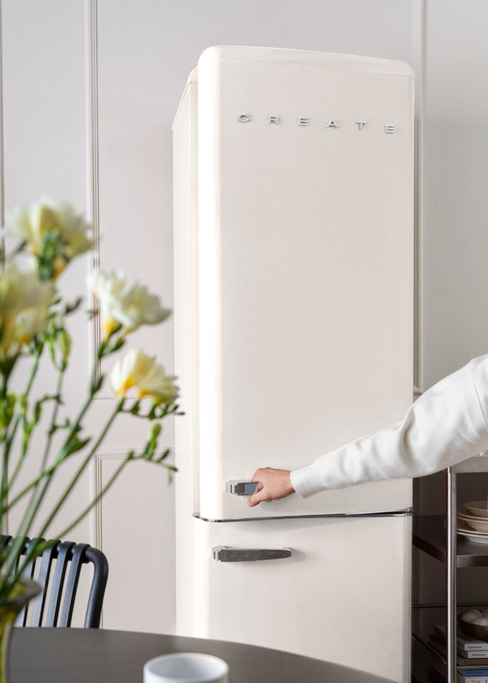 Una mano abre un refrigerador color crema con tiradores plateados.