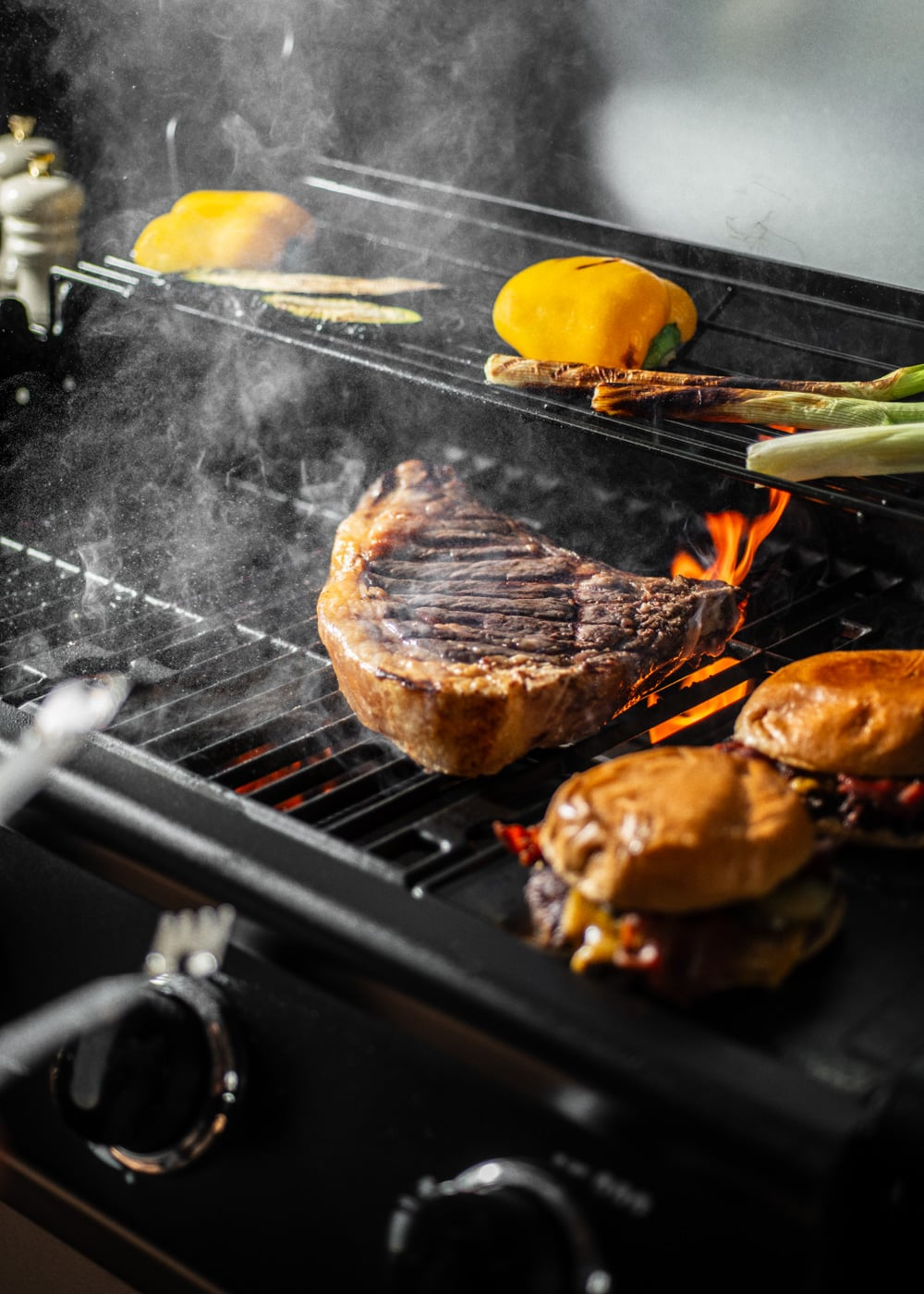 Un gran filete y hamburguesas se asan en una parrilla con llamas.
