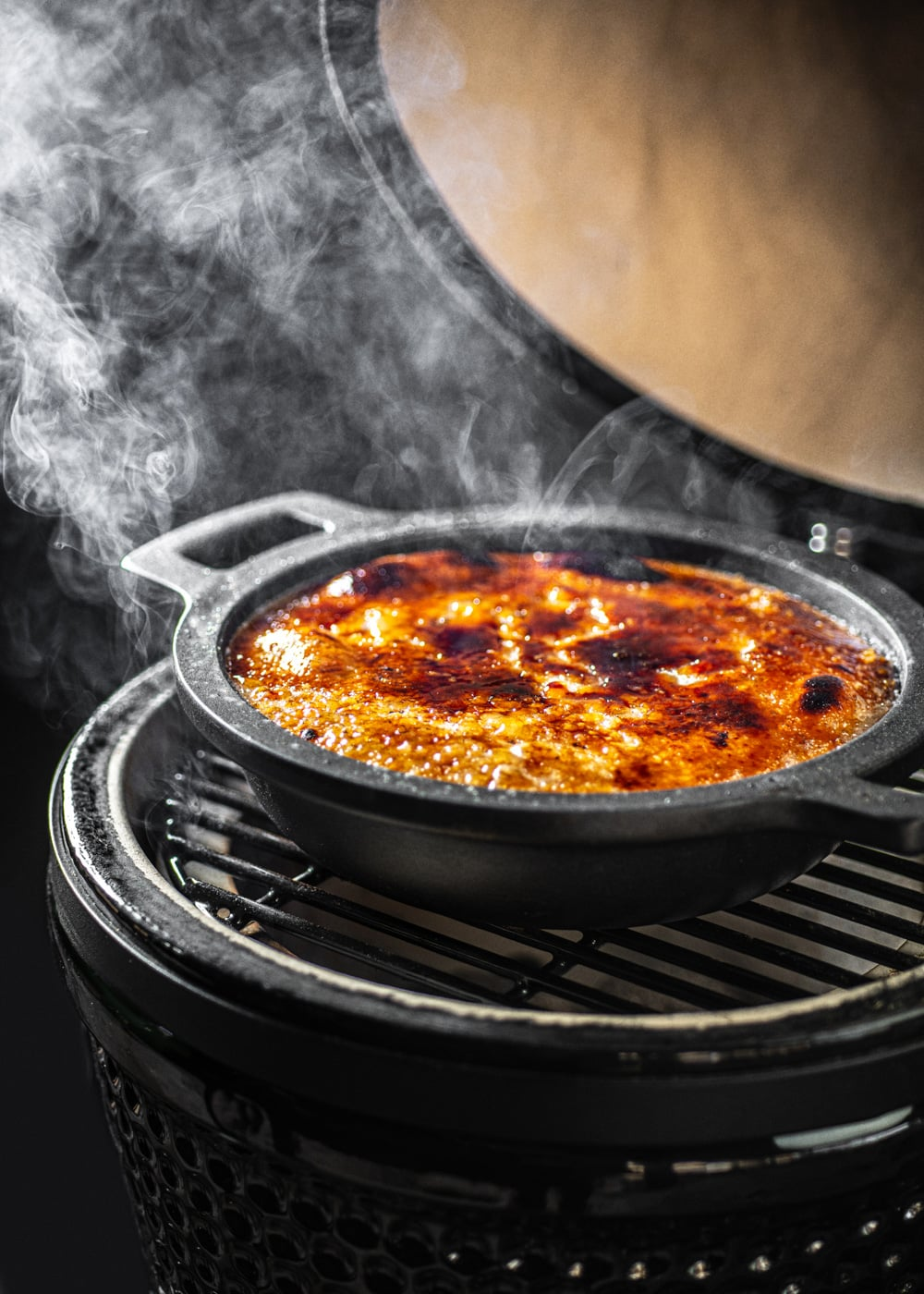 Un crème brûlée en un plato negro sobre una parrilla, con vapor ascendiendo.