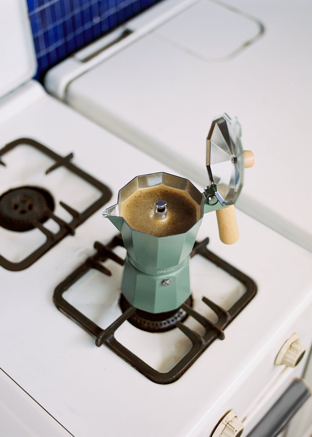 Una cafetera moka verde con café sobre una estufa de gas.