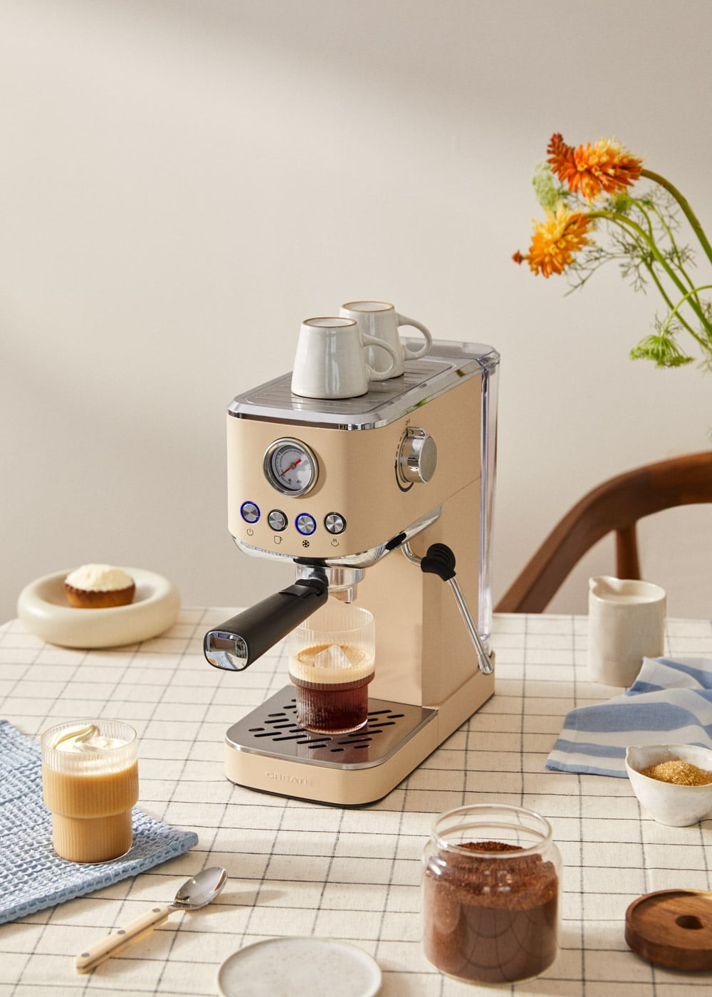 Una cafetera espresso beige con dos tazas encima. Se está preparando café.