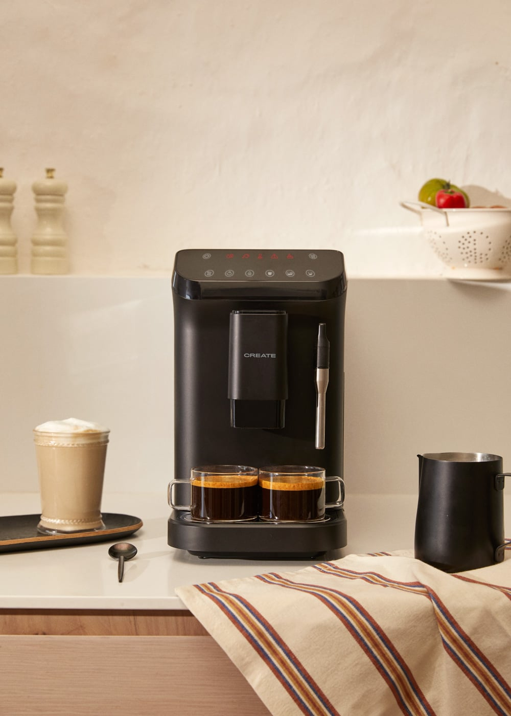 Una cafetera negra con dos tazas de espresso, un café con leche y jarra de leche.