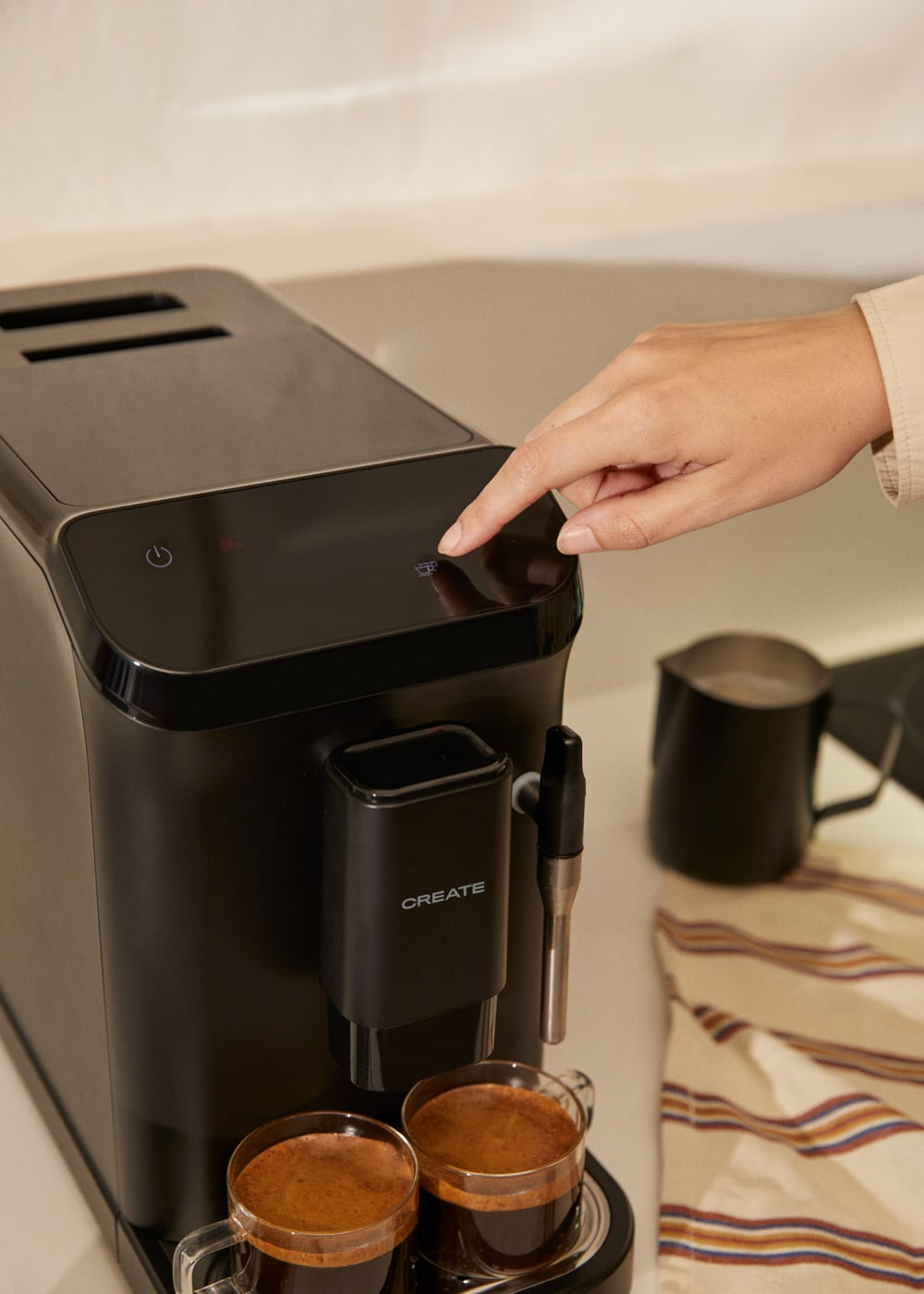 Una mano presiona una cafetera, con dos tazas de espresso delante.