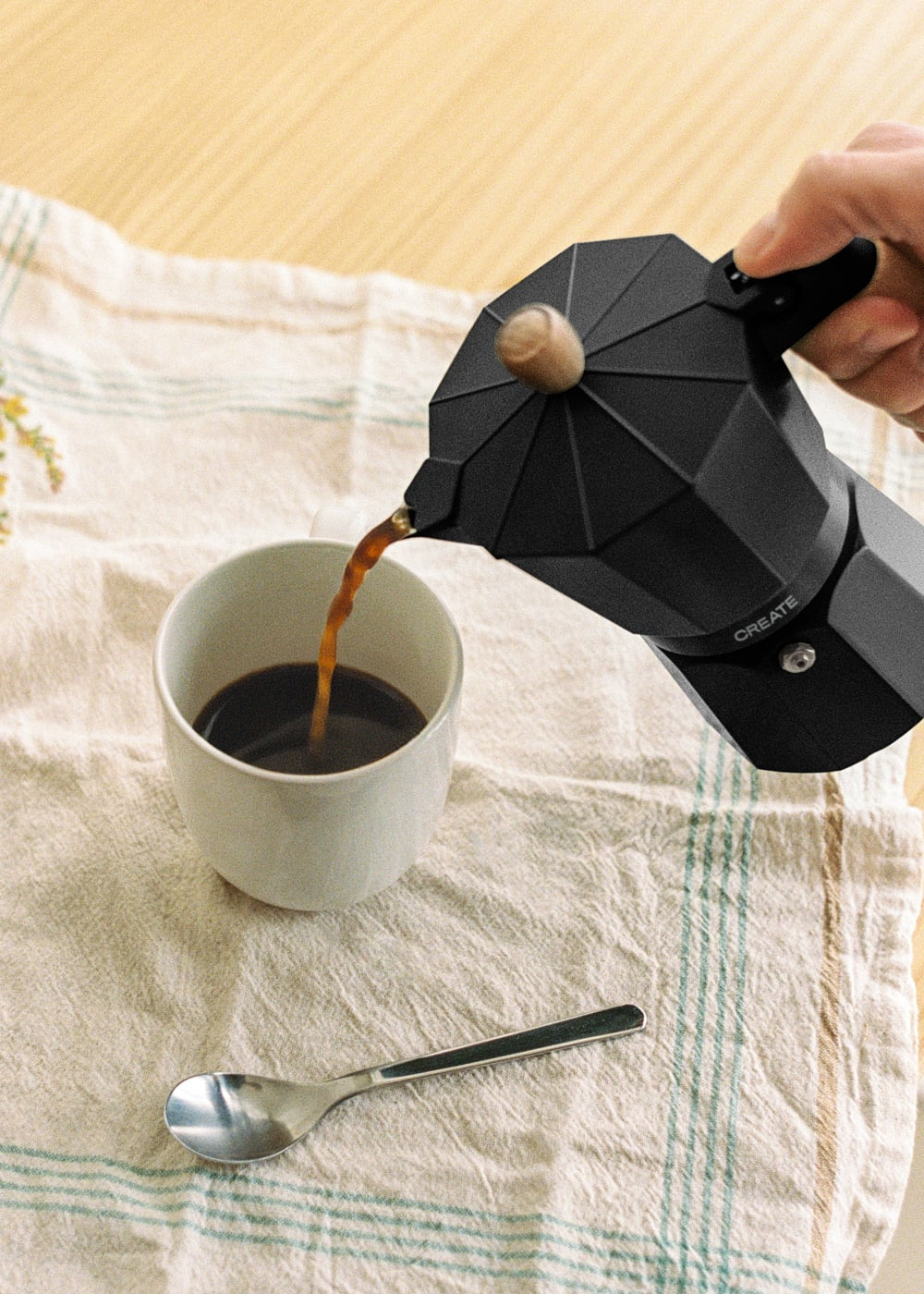 Cafetera moka negra sirviendo café en taza blanca. Una cuchara cerca.