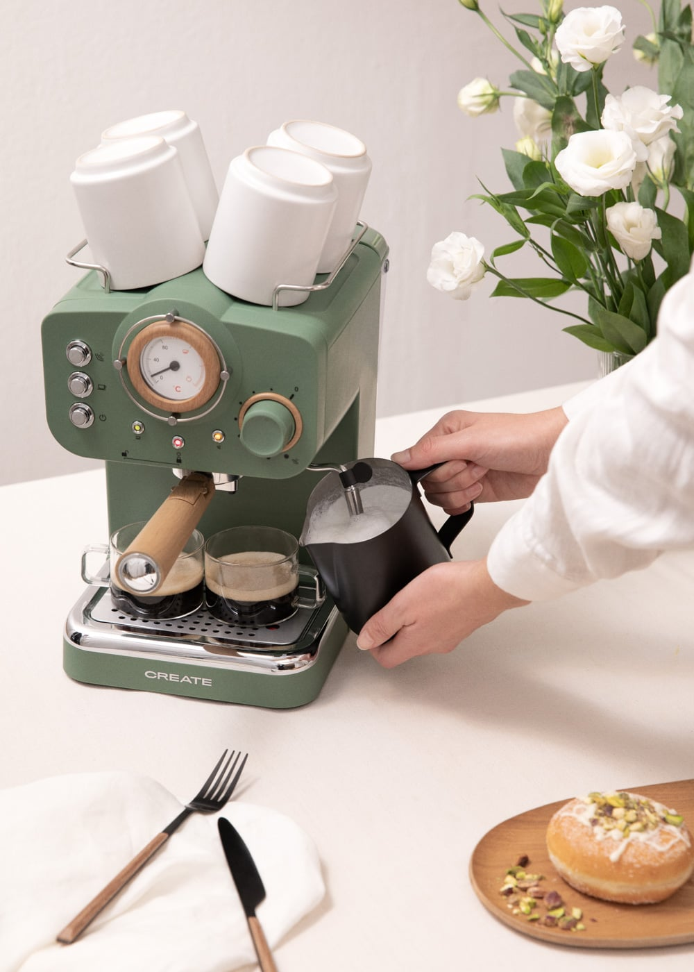 Máquina de espresso verde con jarra de leche, tazas y flores.