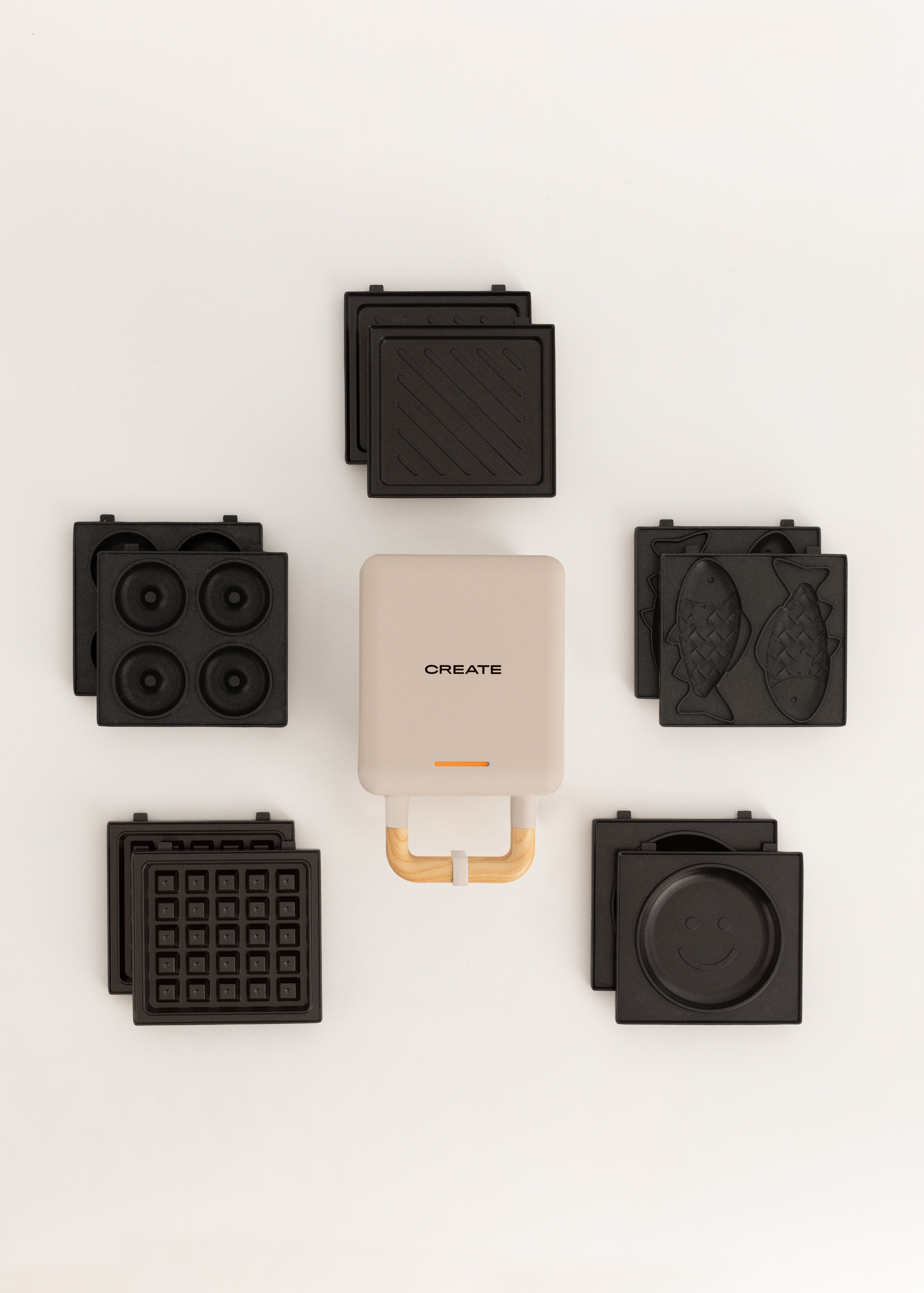 Una sandwichera beige con asas de madera, rodeada de placas de cocina intercambiables.