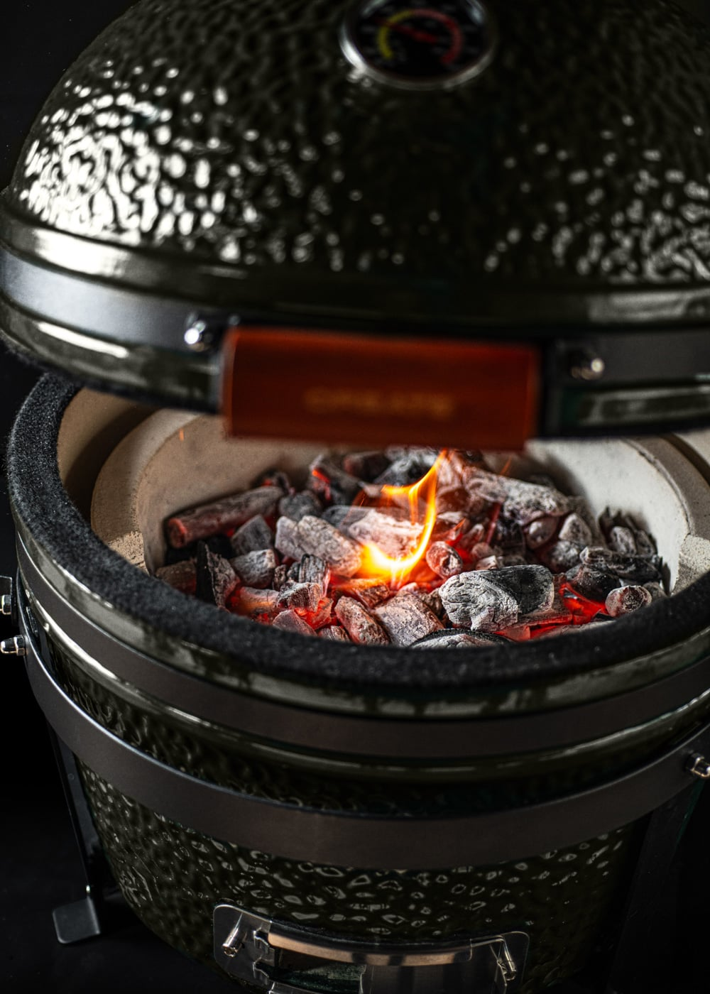 Una parrilla verde de cerámica con brasas incandescentes y llamas dentro.