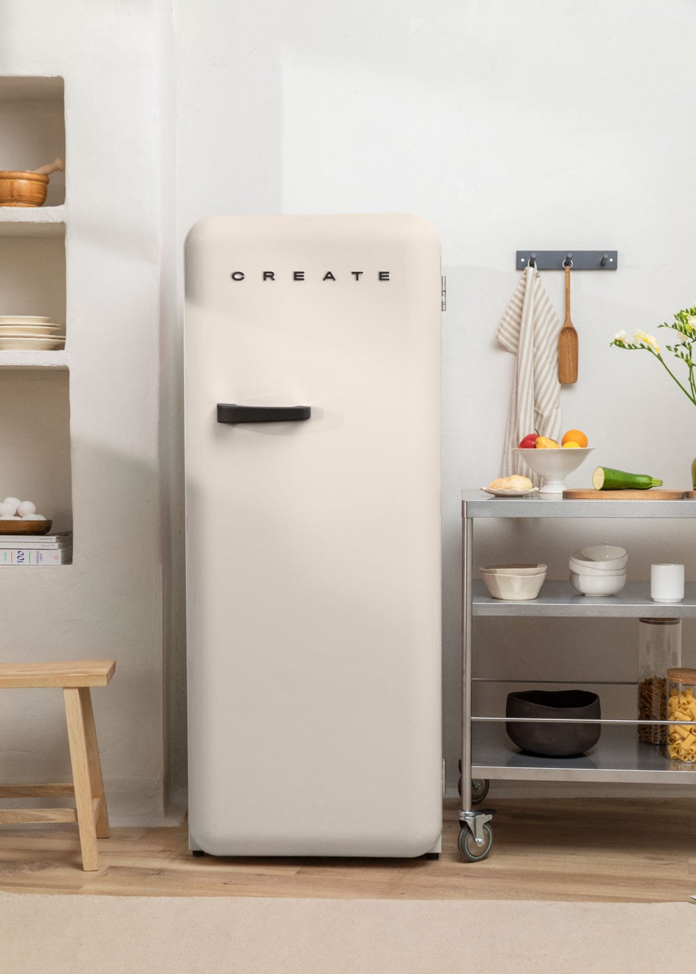 Refrigerador color crema con texto 'CREATE', junto a un carrito metálico con fruta y cuencos.