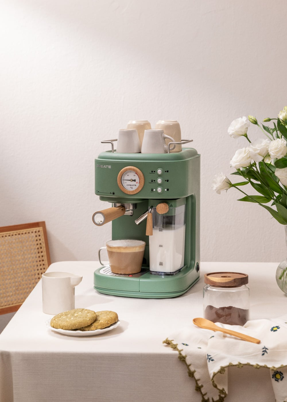 Una máquina de espresso verde con tazas, leche y galletas sobre una mesa.