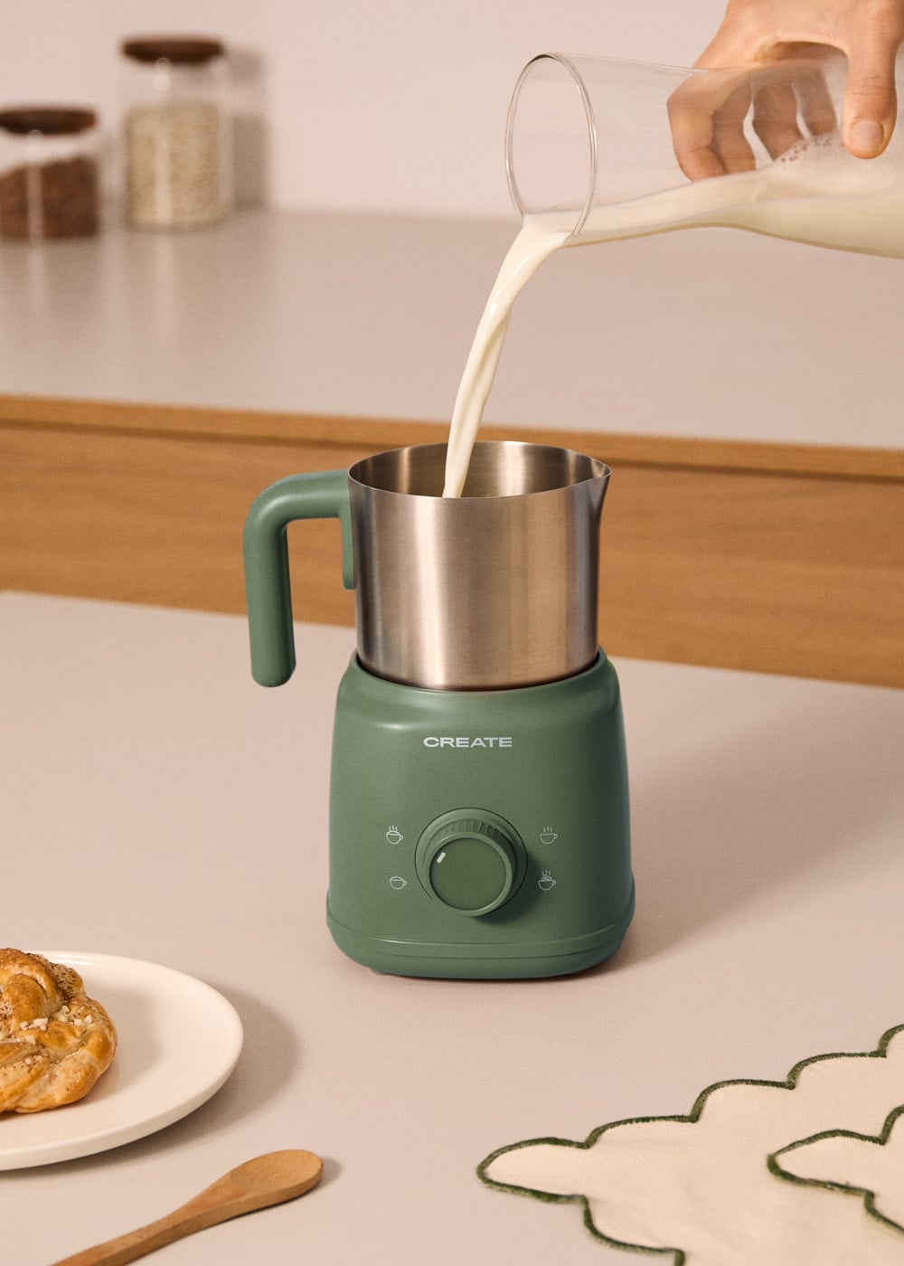 Se vierte leche en un espumador de leche verde, con un pastel cerca.