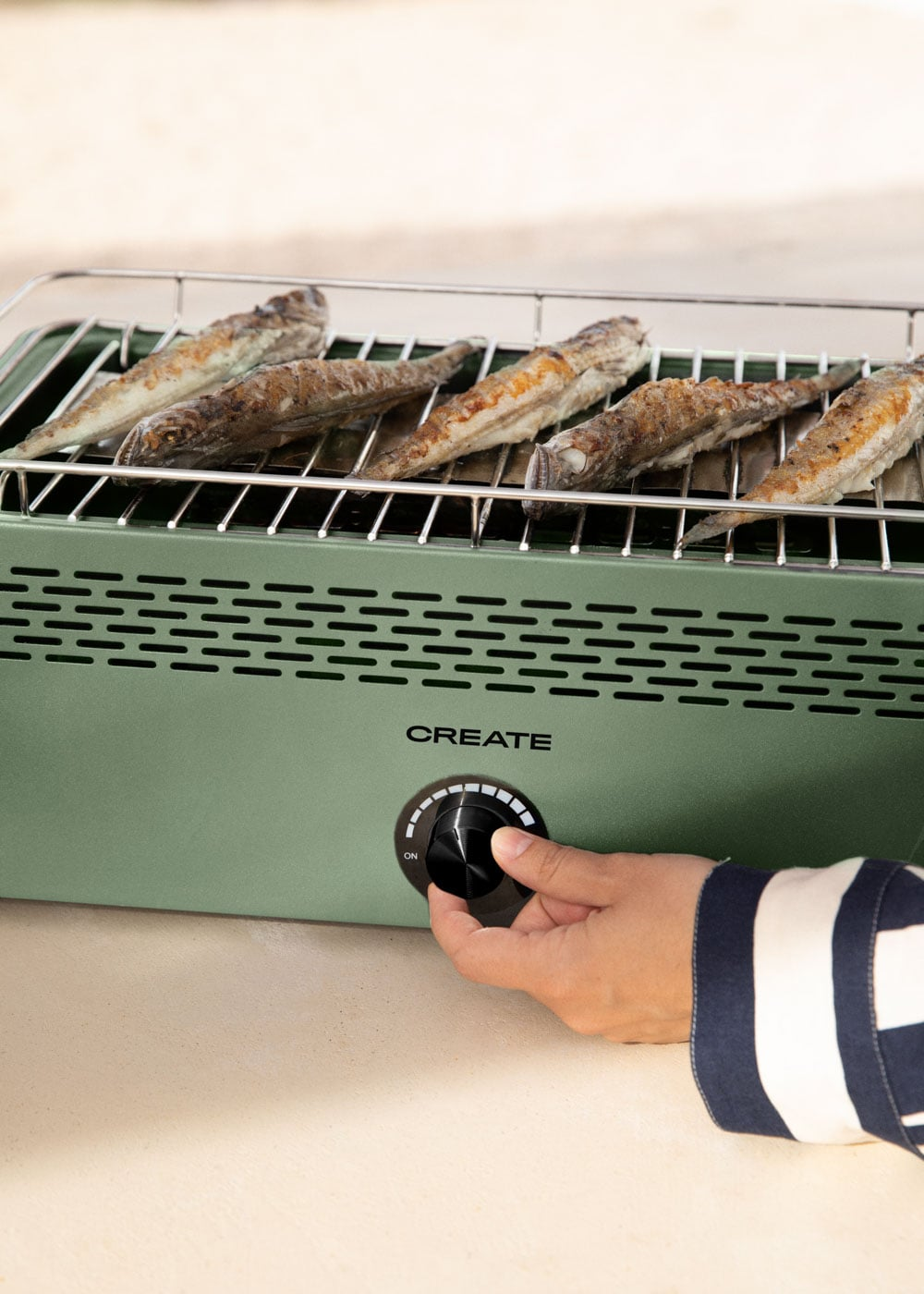 Seis pescados cocinados yacen en una parrilla verde. Una mano gira la perilla.