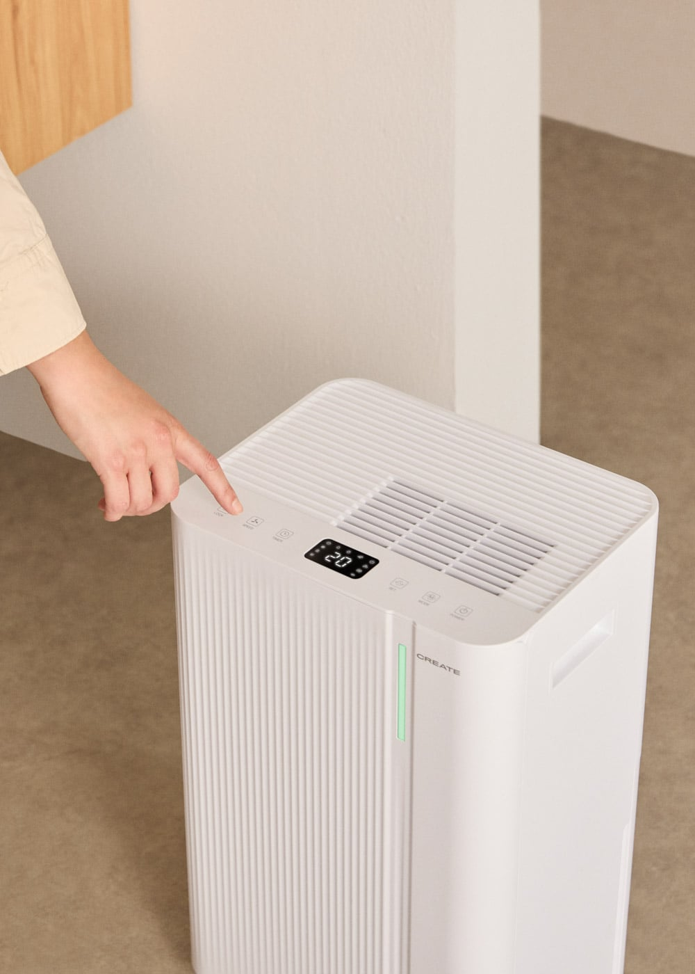 Una mano presiona un botón en un purificador de aire blanco con pantalla digital.