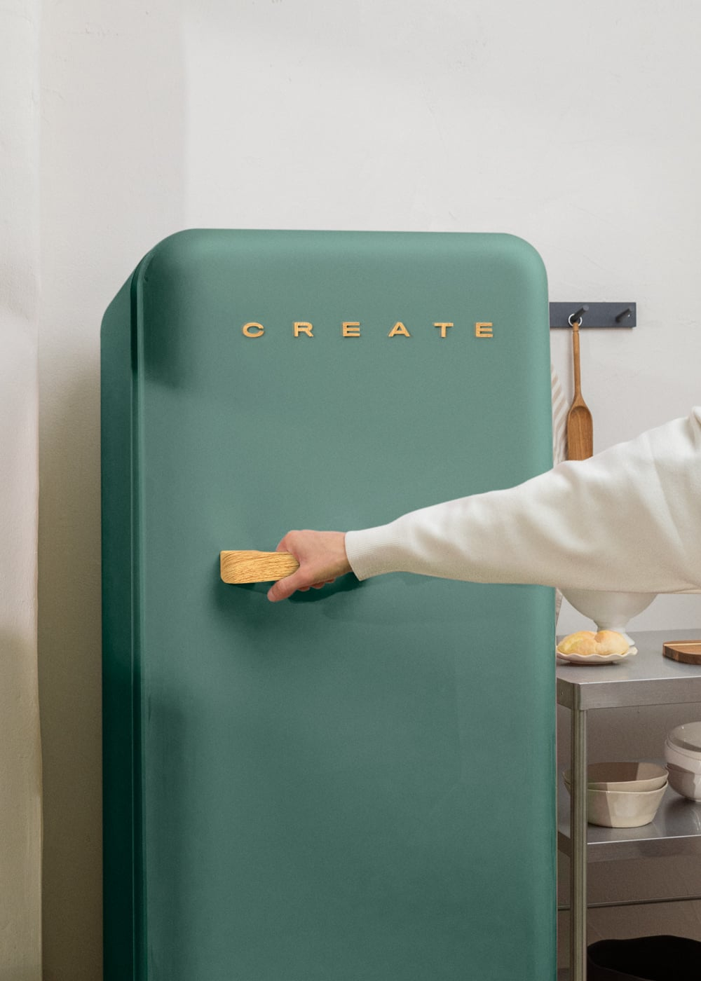 Una mano abre un refrigerador verde con letras doradas.