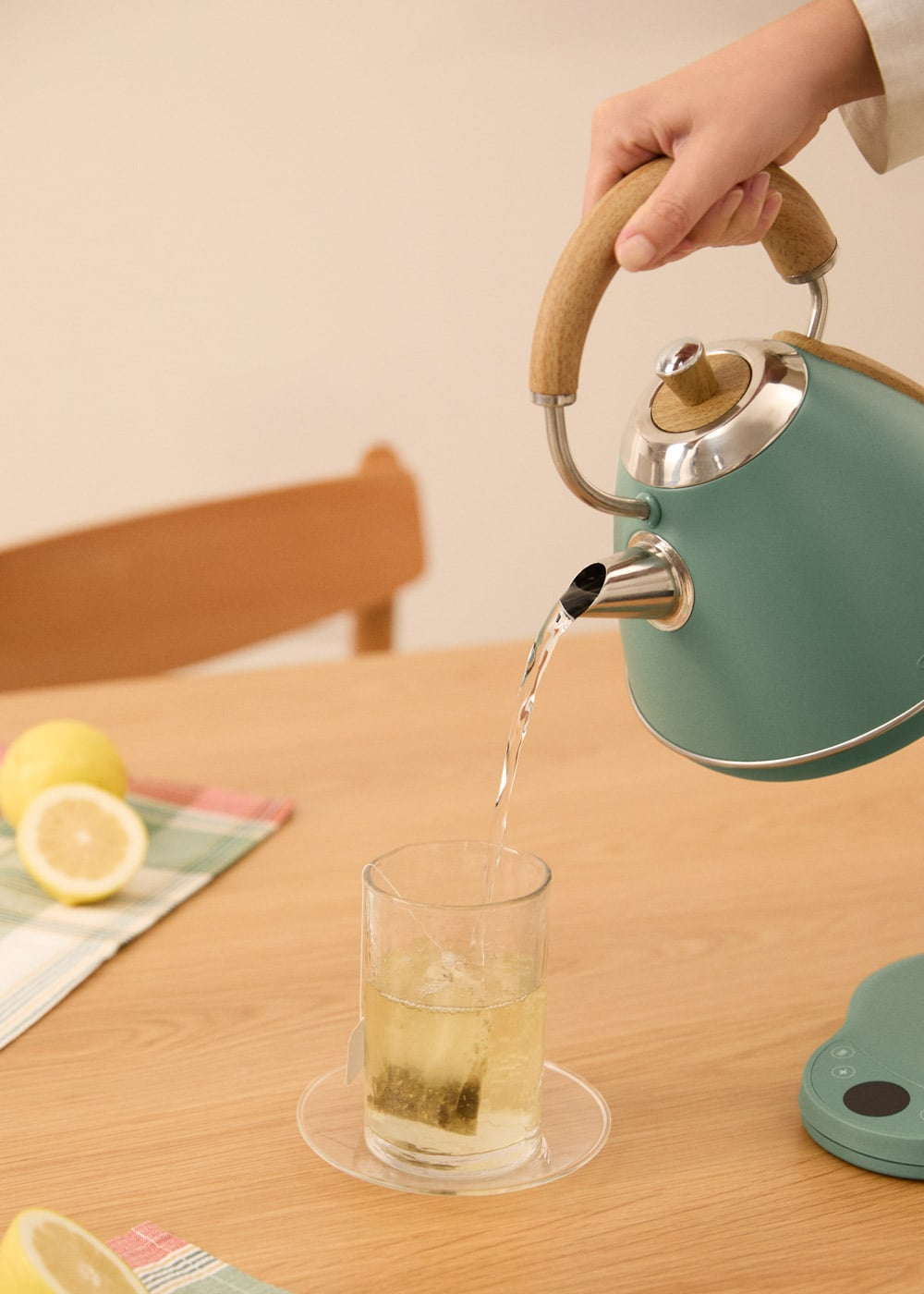 Se vierte agua de una tetera verde azulado con mango de madera en un vaso con bolsita de té.