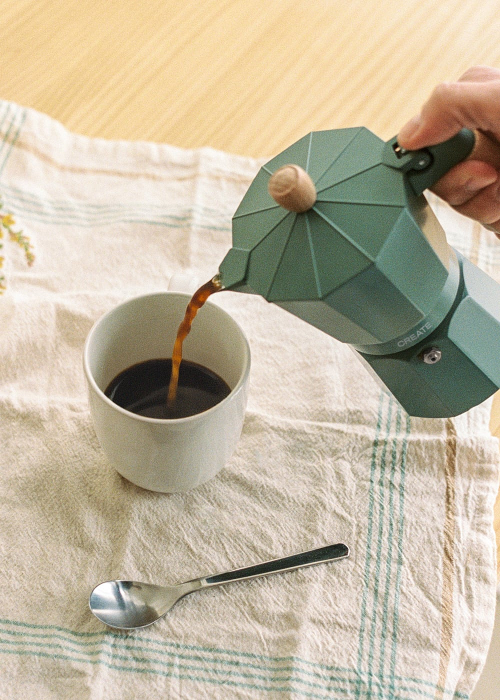 El café se vierte de una cafetera verde a una taza blanca.