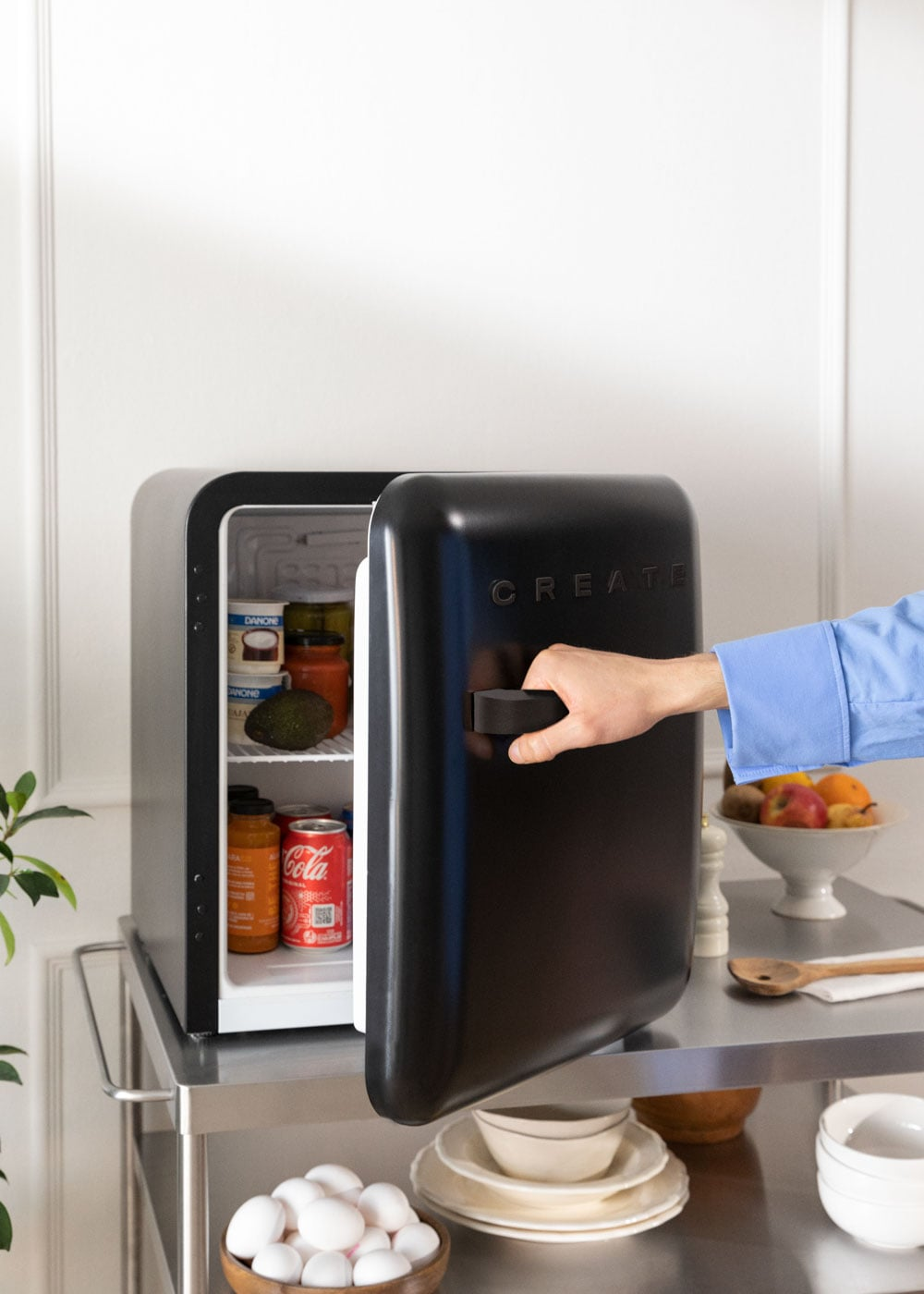 Una mano abre un pequeño refrigerador negro con comida y bebidas.