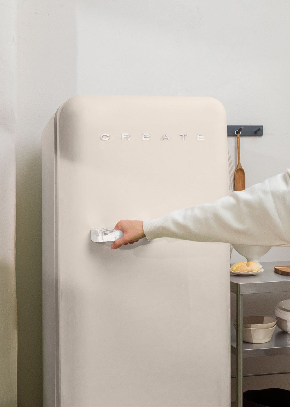 Una mano abre un refrigerador color crema con un asa de mármol.