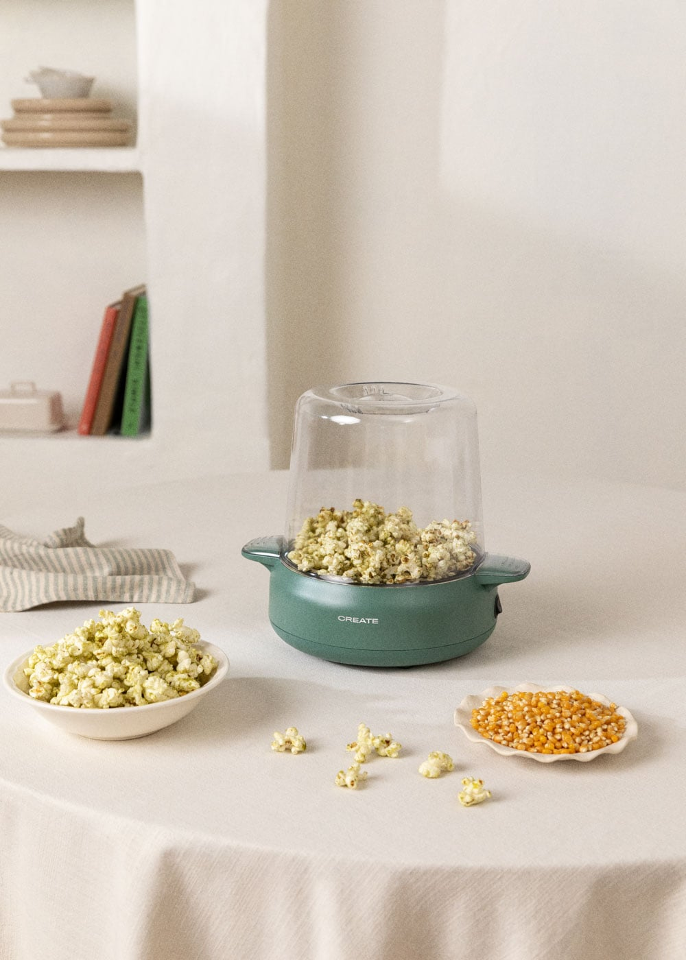 Una máquina de palomitas verde con palomitas y granos de maíz en una mesa.