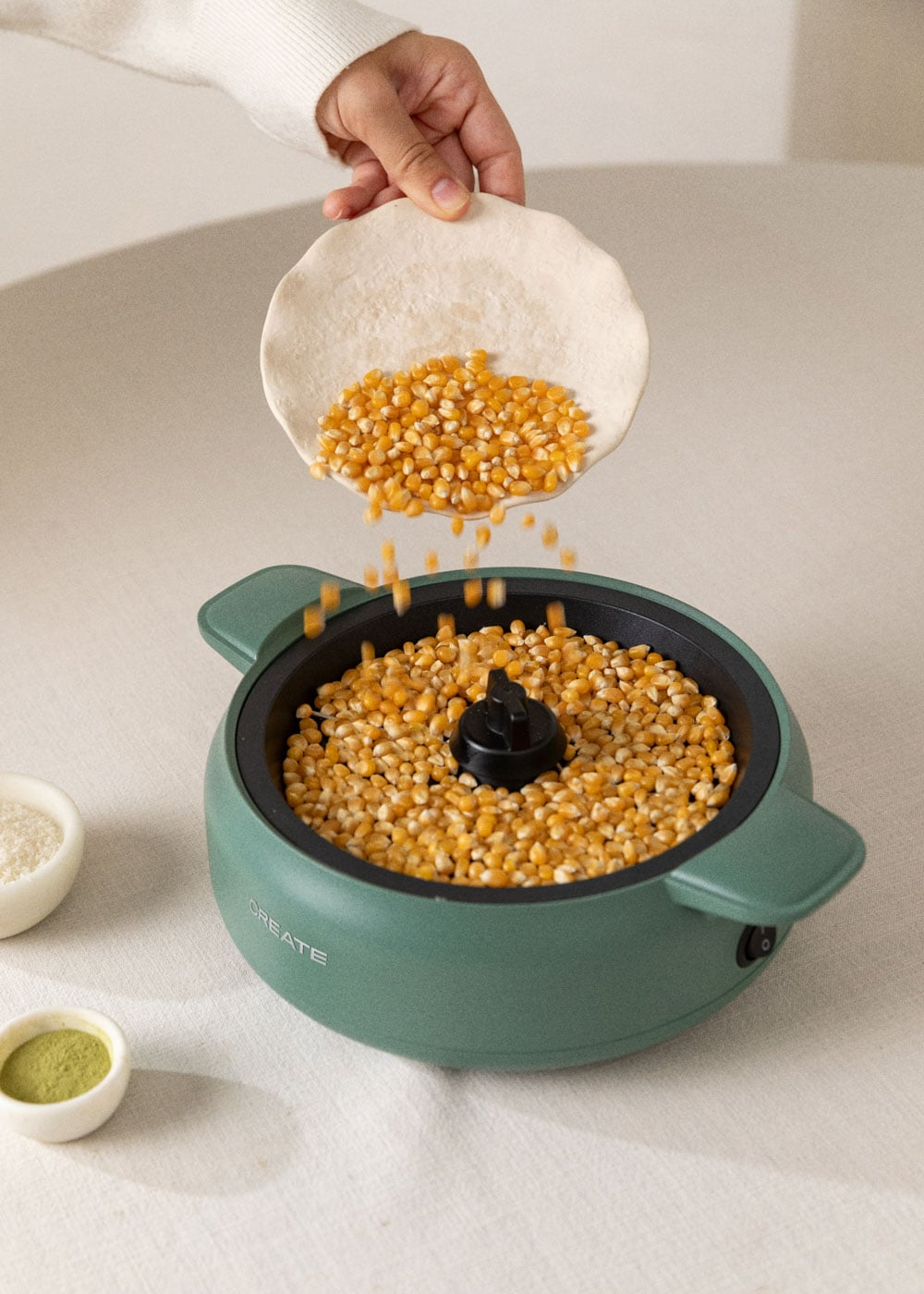 Granos de maíz cayendo de un cuenco a una máquina de palomitas verde.