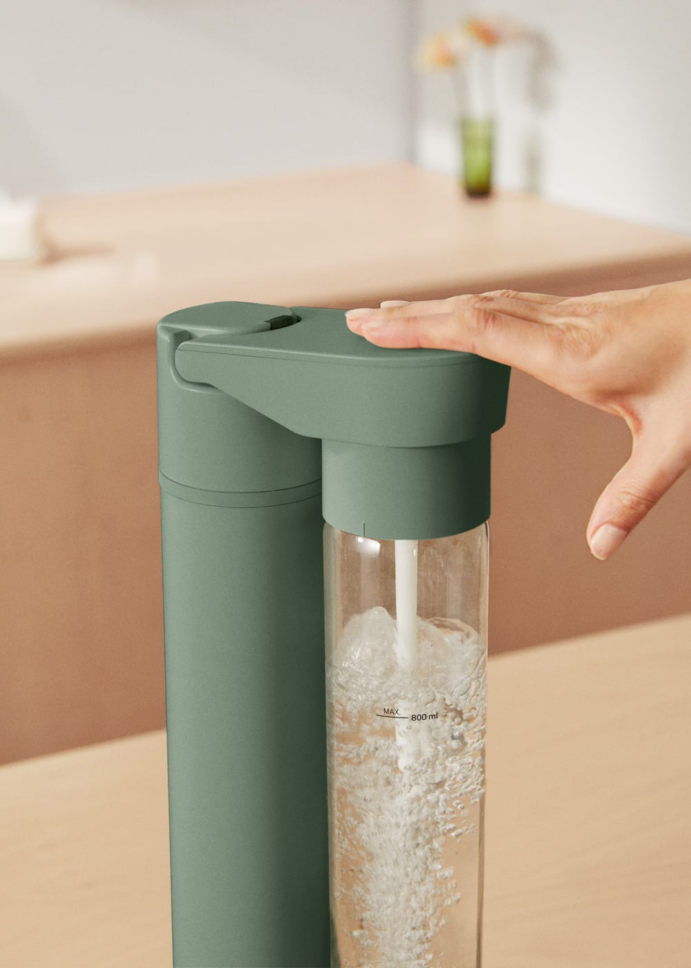 Una mano presiona un carbonatador de agua verde, haciendo burbujas.