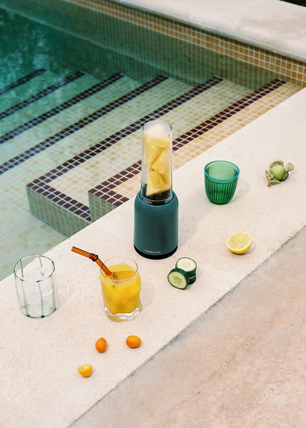 Una licuadora con piña junto a una piscina, con jugo y fruta.