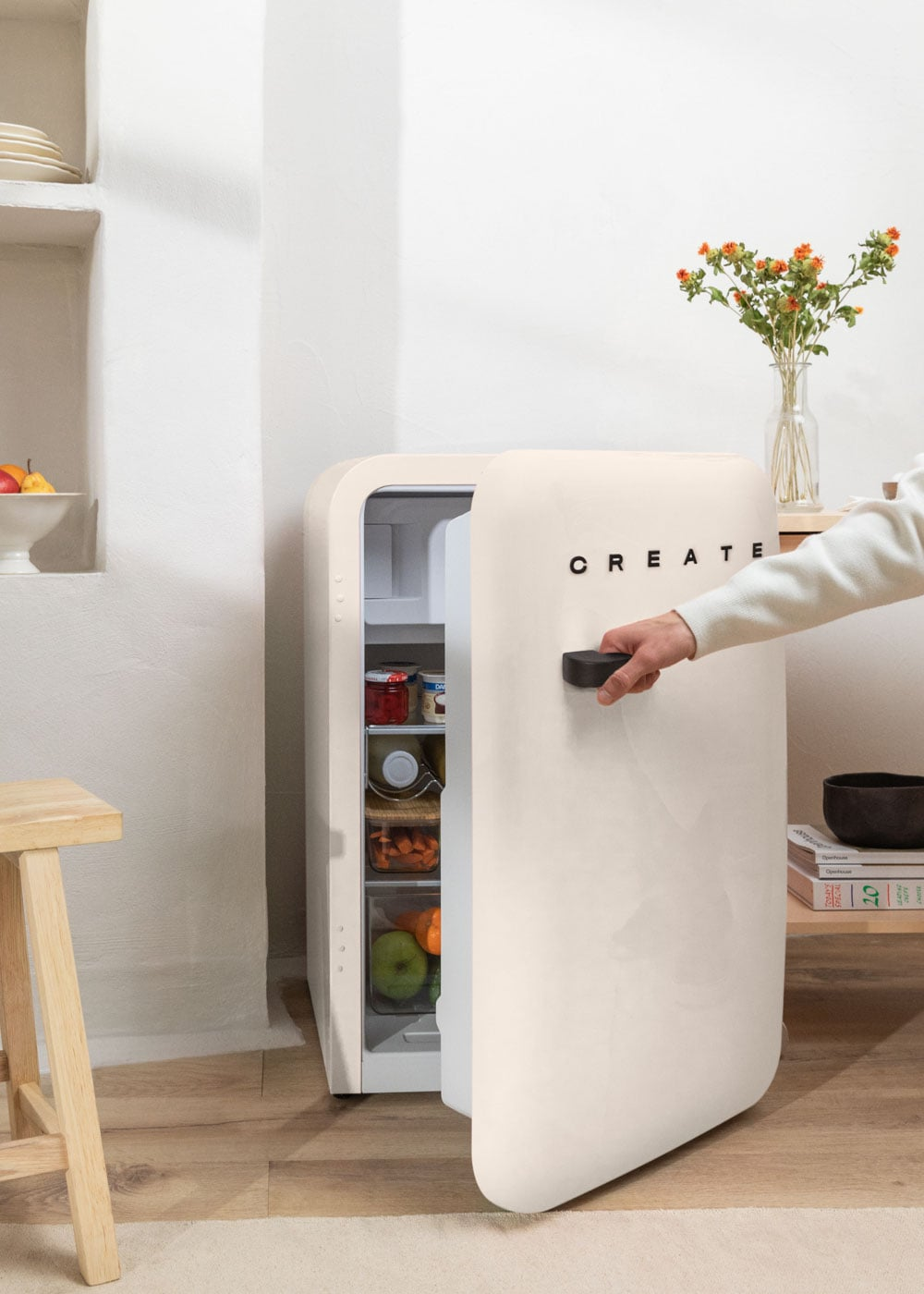 Una mano abre un refrigerador color crema lleno de alimentos.