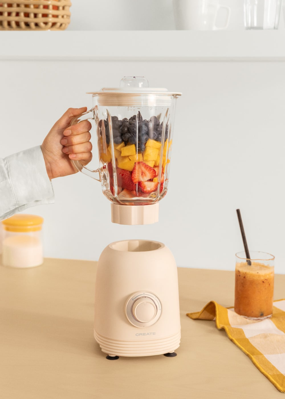 Un vaso de licuadora con fruta se sujeta sobre la base. Un vaso de jugo está al lado.