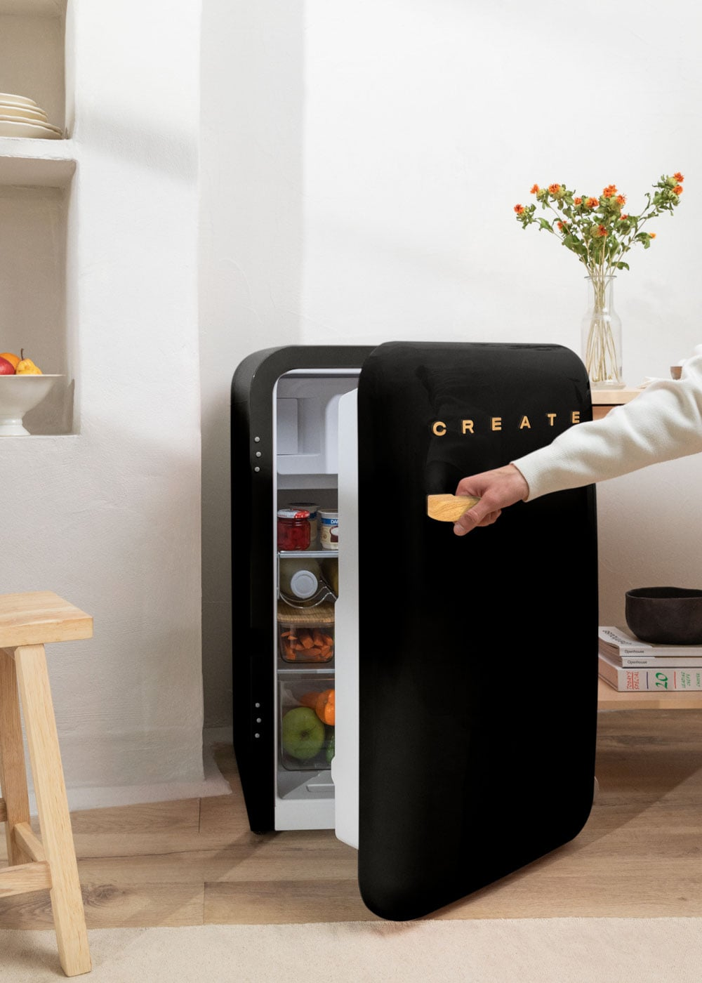 Una mano abre un refrigerador negro con alimentos dentro.