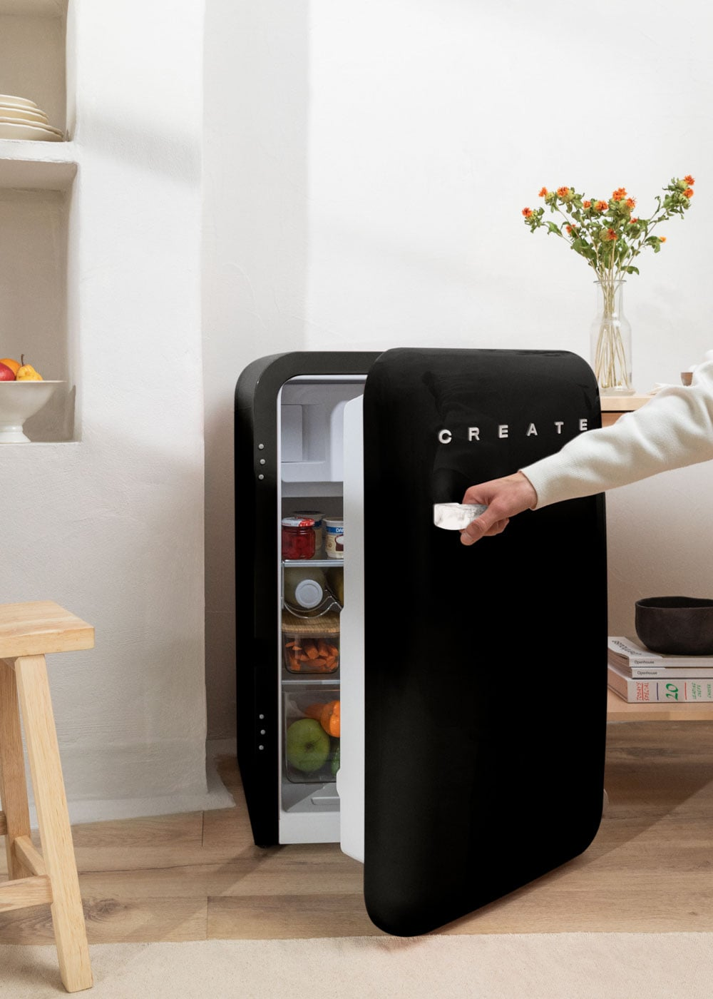 Una mano abre un refrigerador negro que contiene alimentos.