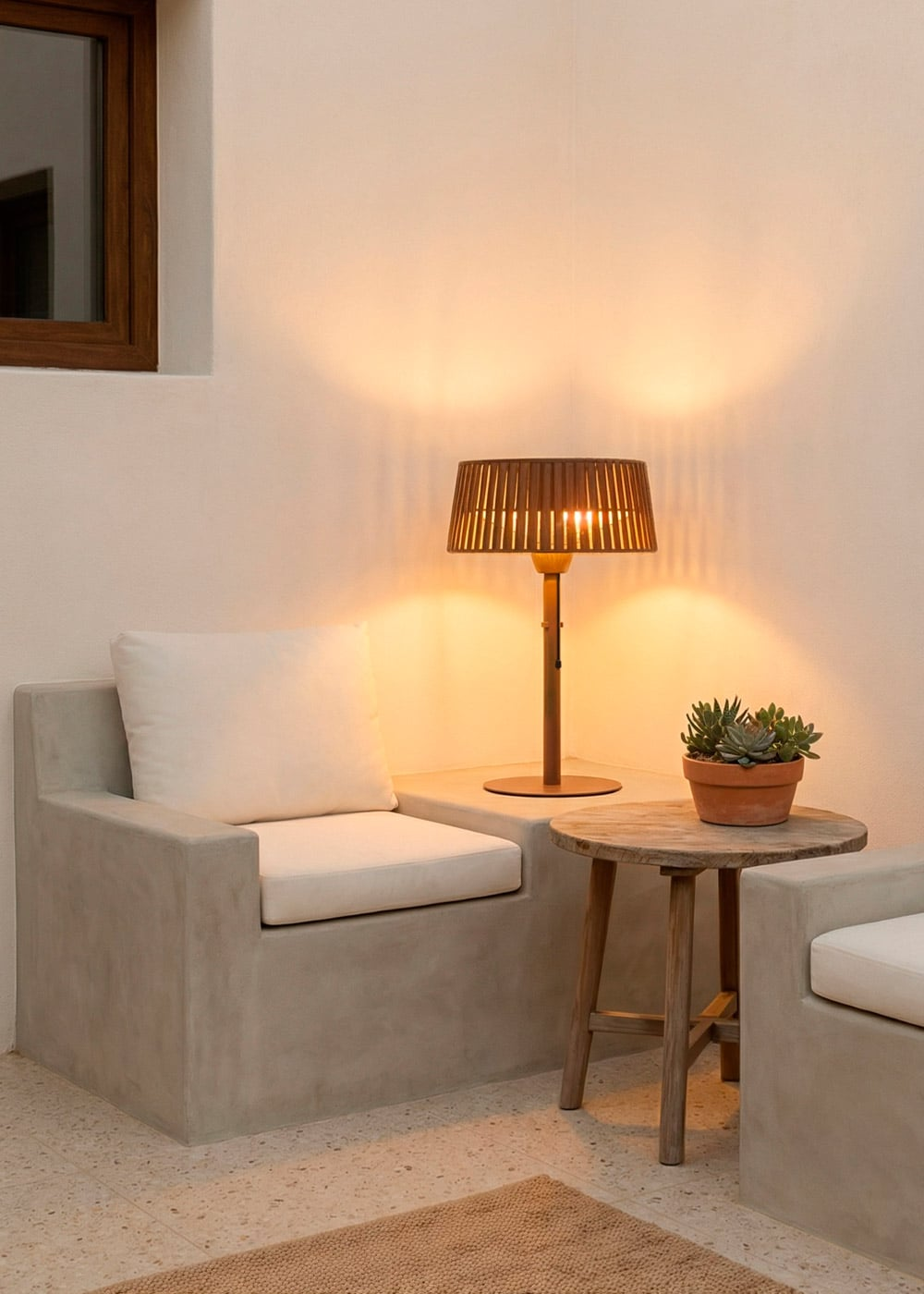 Una lámpara con pantalla de madera está sobre un alféizar de hormigón junto a un sillón blanco.