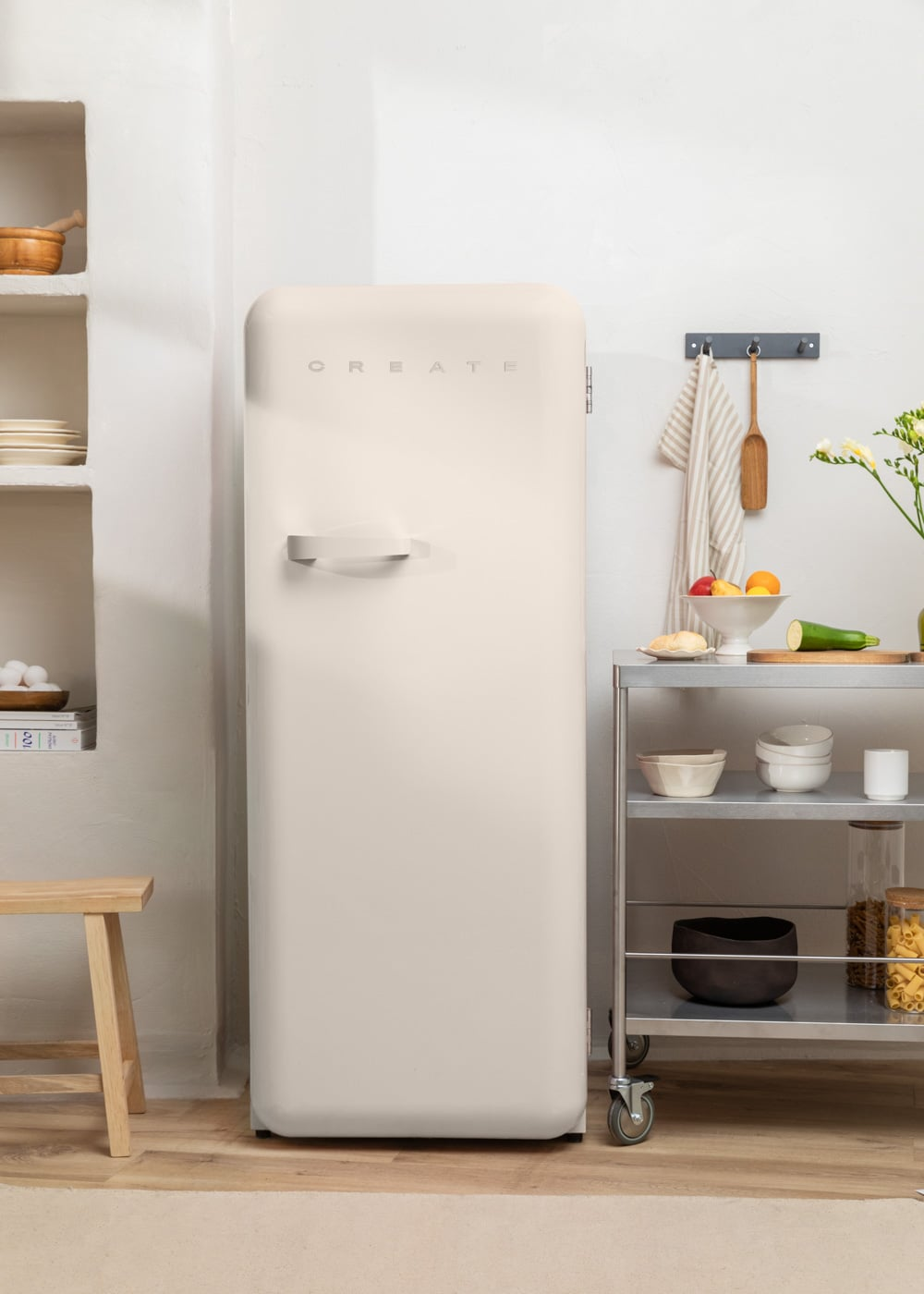 Un refrigerador color crema junto a un carrito metálico con fruta y cuencos.