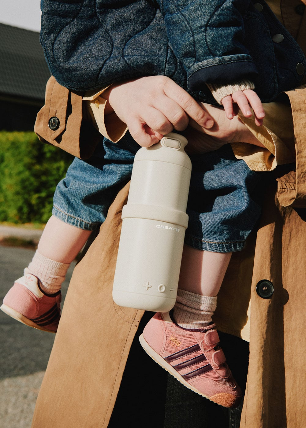 Niño con botella beige, llevado por persona con jeans y abrigo.
