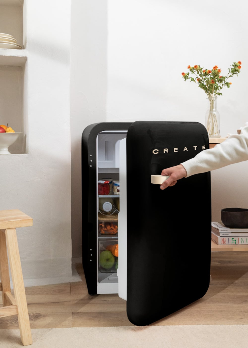 Una mano abre un refrigerador negro con comida dentro.
