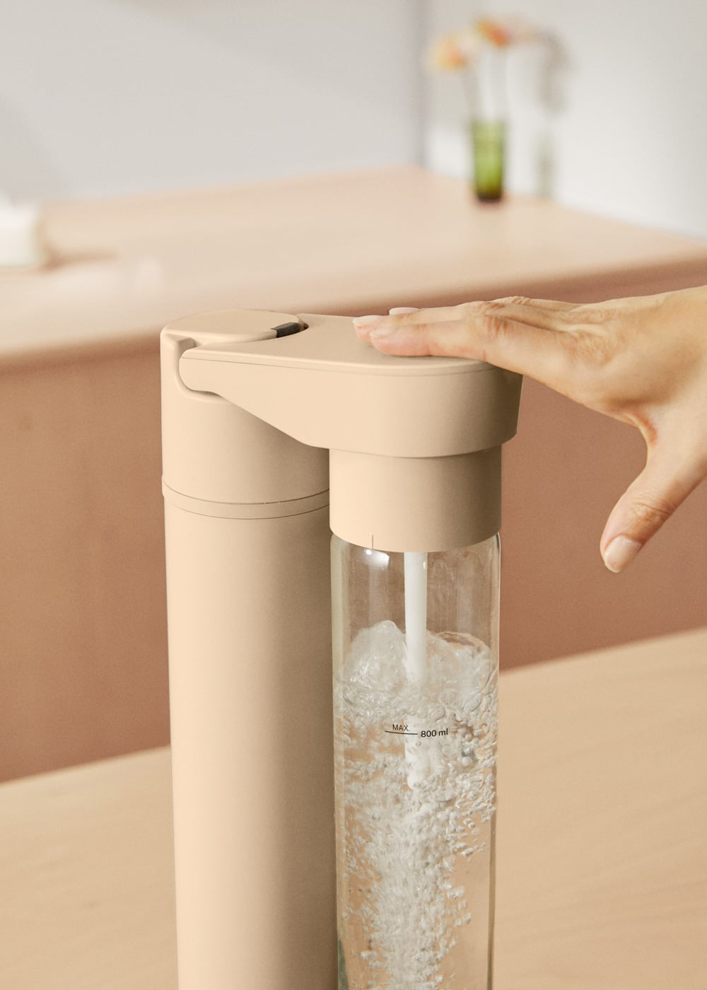 Mano presionando un carbonatador de agua beige, burbujas suben en la botella.