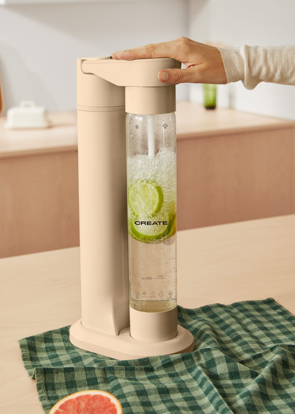 Una mano presiona un carbonatador de agua beige con una botella llena con rodajas de lima.