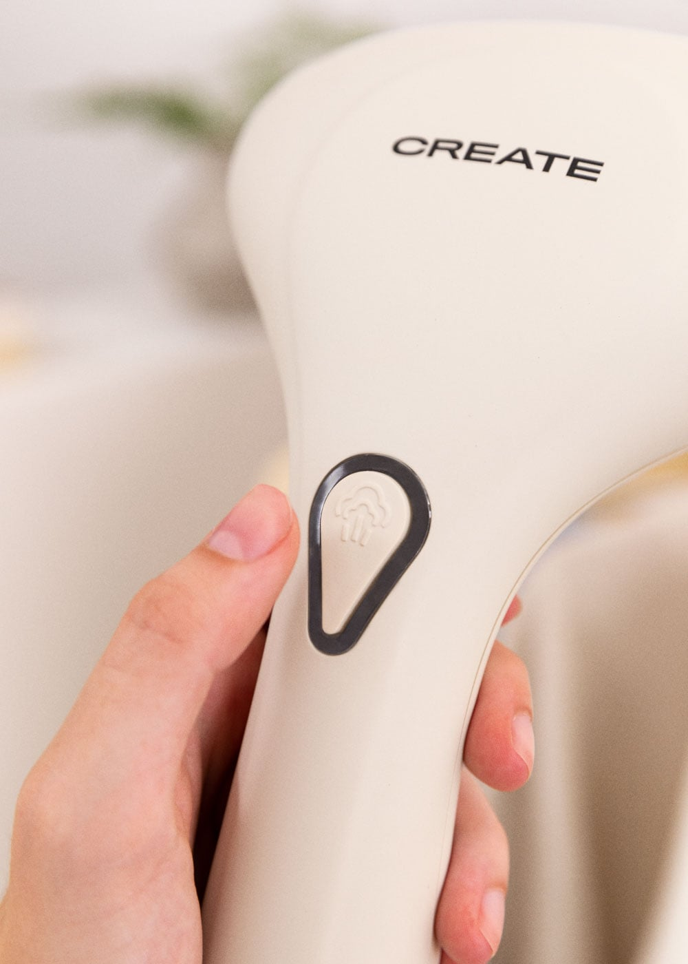 Una mano presiona un botón de vaporizador de mano beige con icono de vapor. Logo CREATE visible.
